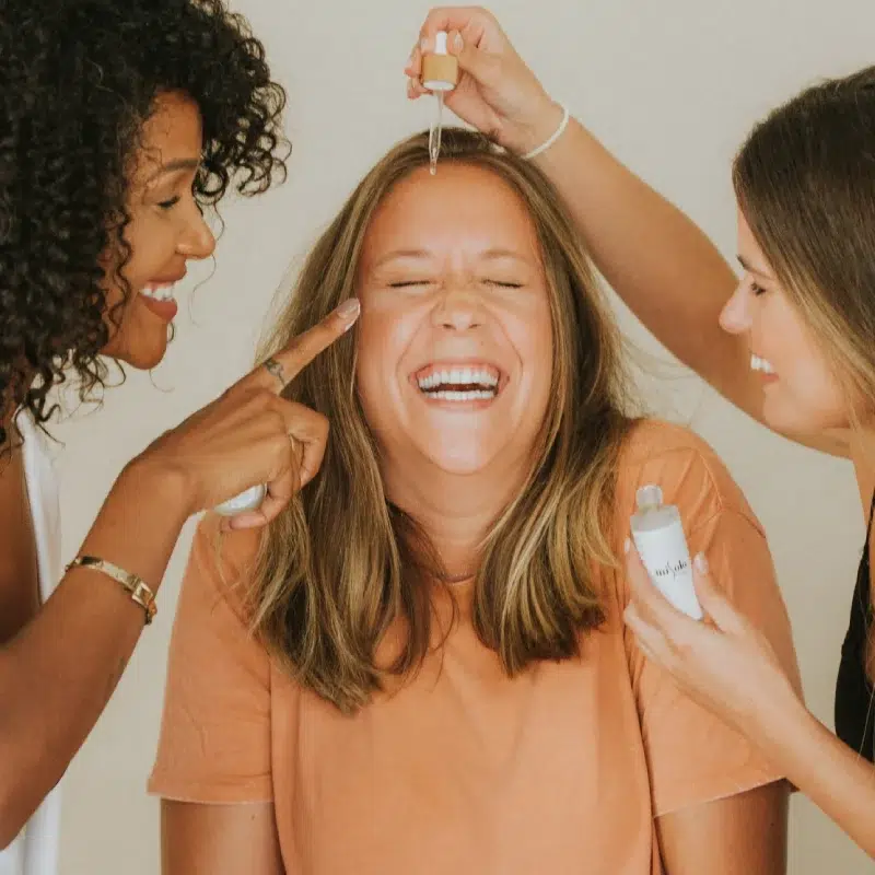 Trois femmes souriantes appliquent du sérum
