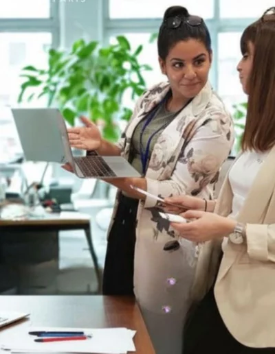 Deux femmes discutant au bureau avec un ordinateur portable.